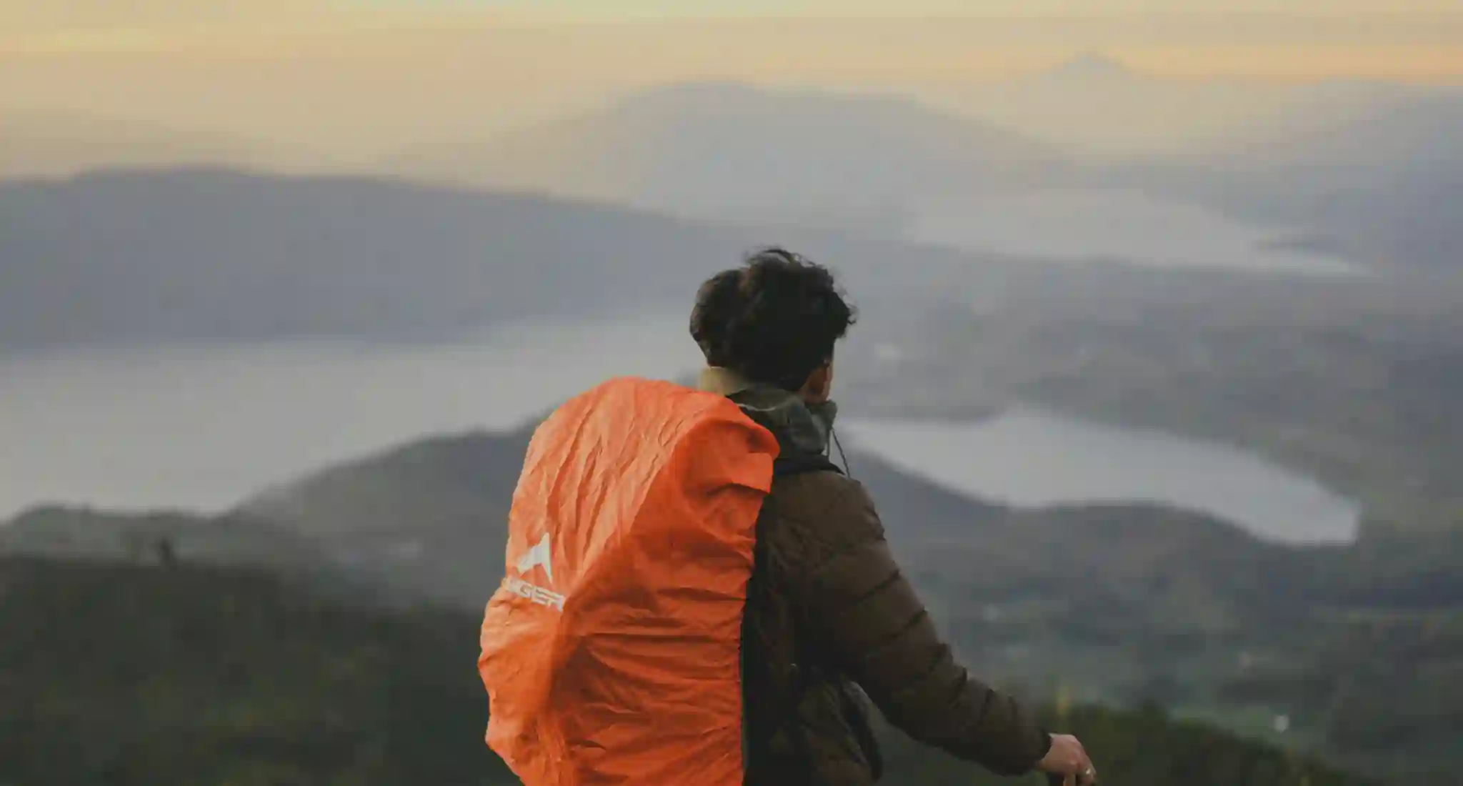 Petualang dengan carrier orange melihat panorama gunung